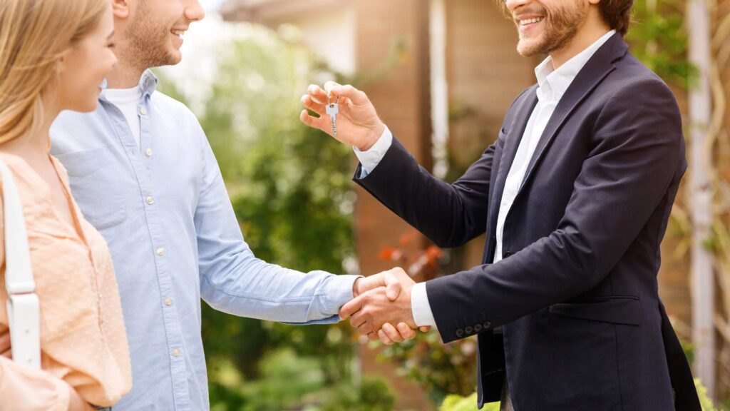 Immobilienmakler uebergibt Schluessel an Paar beim Hauskauf in Deutschland